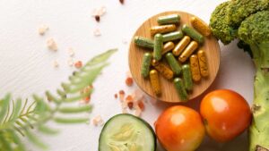 Supplements for gut health including probiotic capsules, on a wooden plate along with some healthy foods.